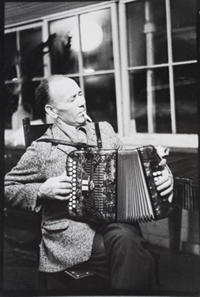 Joe Cooley playing his accordion, his eyes closed and a cigarette in his mouth.